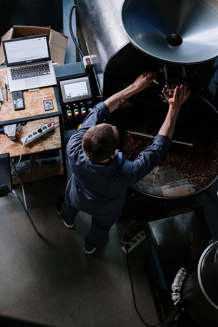 A man processes coffee beans in a roaster, managing settings in a modern workshop environment.